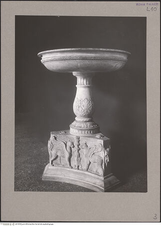 Vorderseite von Archivio Fotografico Musei Vaticani [https://www.deutsche-digitale-bibliothek.de/content/lizenzen/rv-ez/] Antike sechseckige, konkav geschwungene Basis mit Greifmotiv und Bucranium auf modernem Sockel, darauf moderne Brunnenschale - Gesamtansicht, bh102393_recto. Foto.