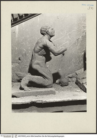 Vorderseite von ICCD [https://www.deutsche-digitale-bibliothek.de/content/lizenzen/rv-ez/] Mittelportal mit Dreiecksgiebel über kompositen DreiviertelsäulenMadonna, flankiert von zwei knienden Gestalten - Linke kniende Figur, rechtes Körperprofil, bh219302_recto. Foto.